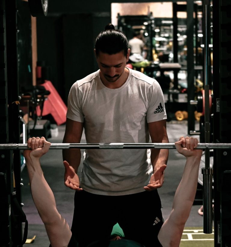 Mirko unterstützt einen Athleten beim Bankdrücken im Fitnessstudio.